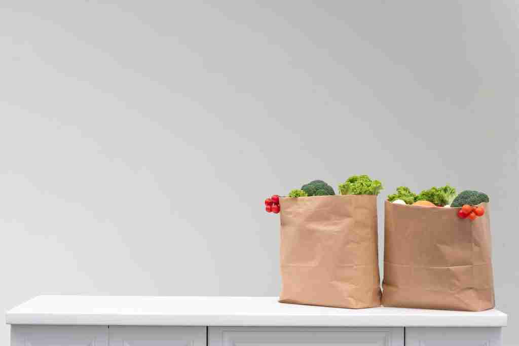 Reusable grocery bags with vegetables and simple travel food essentials on a kitchen table